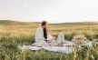 a man and woman sitting on a blanket in a field